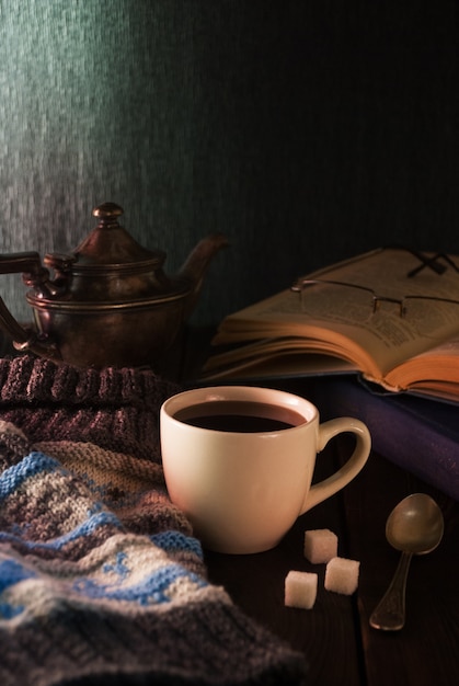 Taza de té, libro y gorro de lana sobre una mesa de madera