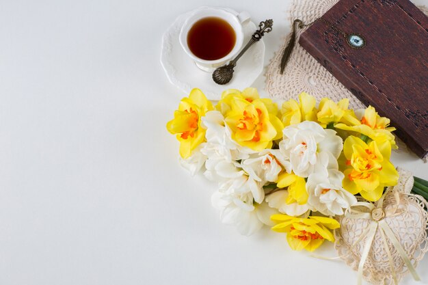 Una taza de té, un libro, un ramo de narcisos y un corazón de encaje.