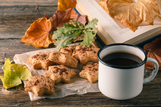 Taza de té con el libro viejo, hojas de otoño en la mesa de madera.