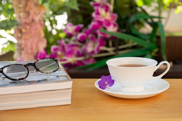 Taza de té con los libros y los vidrios de los ojos en la tabla de madera en jardín.