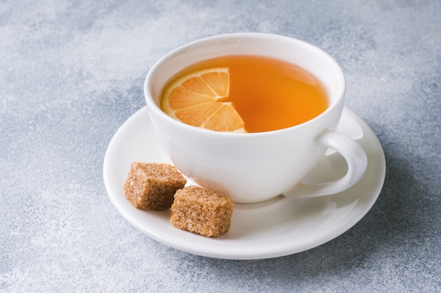 Taza de té con limón y azúcar morena sobre la mesa.