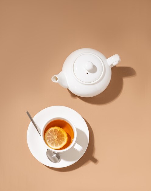 Una taza de té con limón y una cuchara sobre un fondo claro con una tetera blanca Concepto de bebida saludable por la mañana Vista superior y espacio de copia