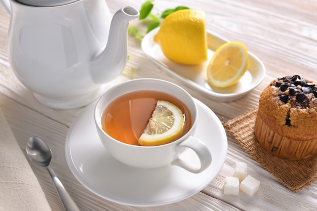 Taza de té con limón y cupcake en mesa blanca