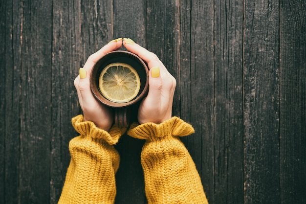 Taza de té con limón en una mano femenina.