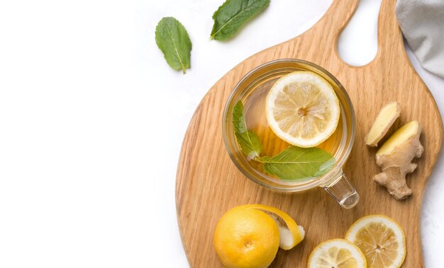 Taza de té con limón, menta y jengibre de cerca en blanco