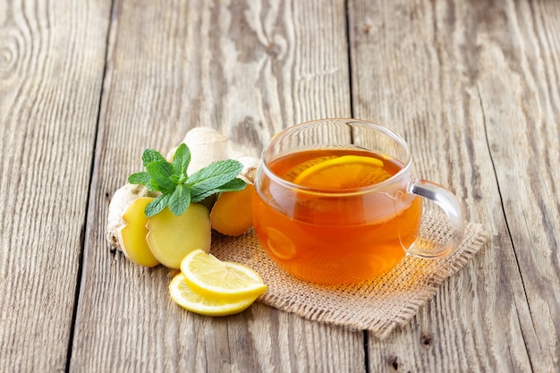 Una taza de té con limón, menta y jengibre en la mesa rústica de madera.