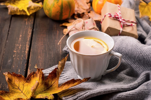 Taza de té con limón en la mesa de madera oscura con hojas de otoño