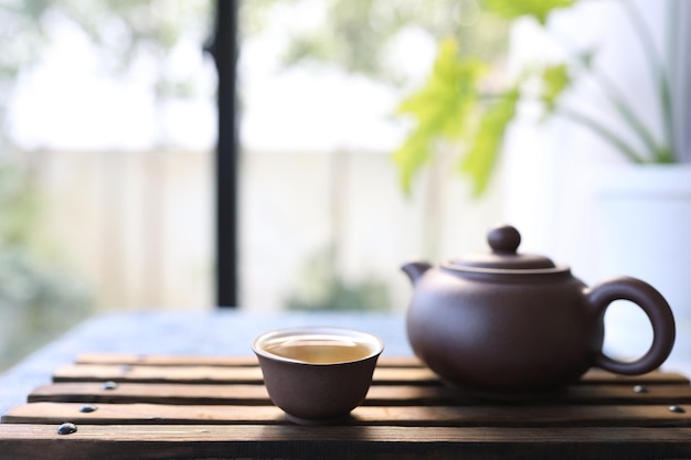 Taza de té de loza y tetera en bandeja de madera