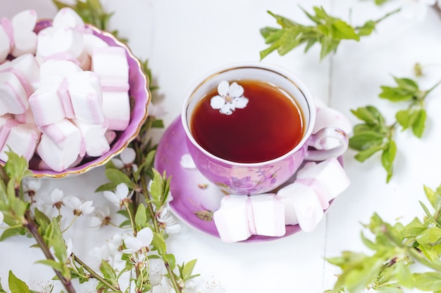 Una taza de té con malvavisco rosado y blanco con ramita de flor de manzana