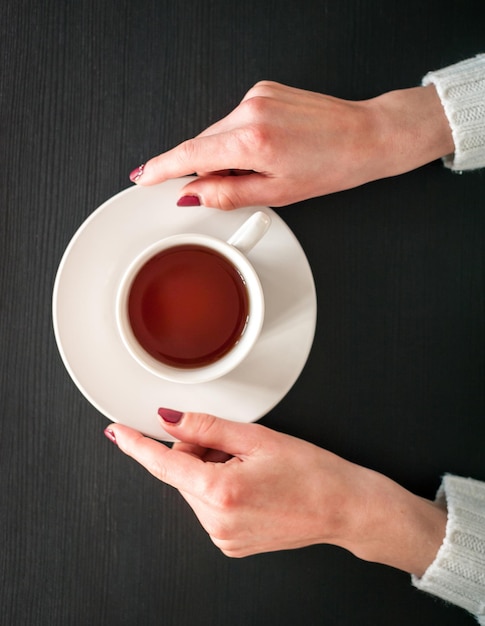 Taza de té de la mañana en manos de una mujer joven