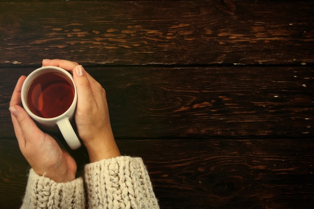 Taza de té en las manos sobre un fondo de madera el concepto de un otoño acogedor