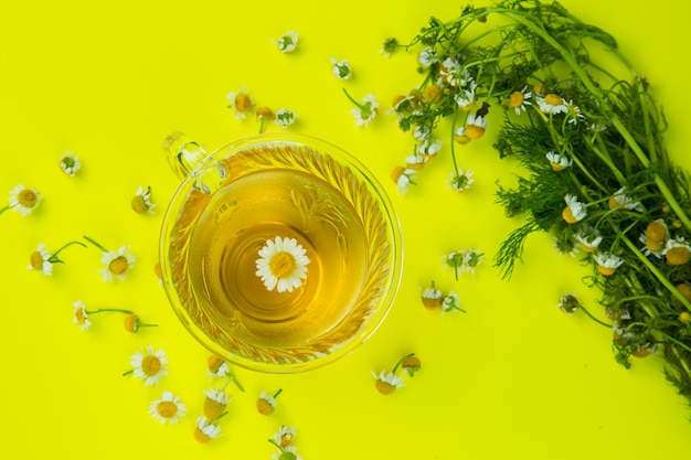 Taza de té de manzanilla con flores de manzanilla en fondo amarillo