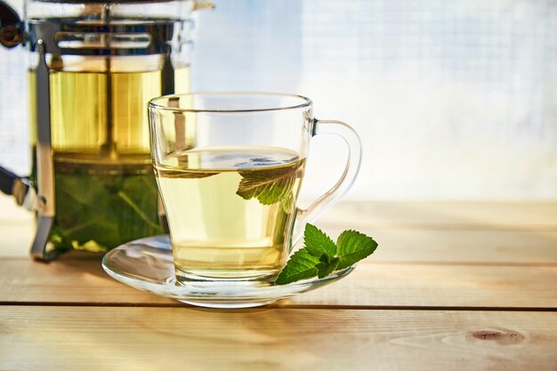 Una taza con té de menta aromático fresco sobre una mesa de madera con el telón de fondo de una ventana