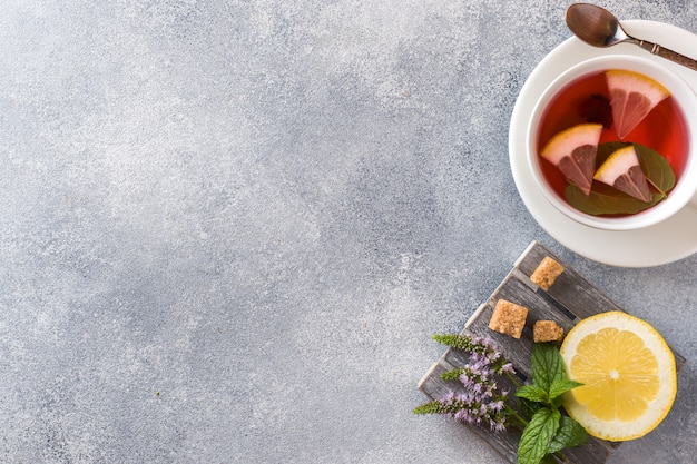 Taza de té, menta y limón en mesa gris con espacio de copia