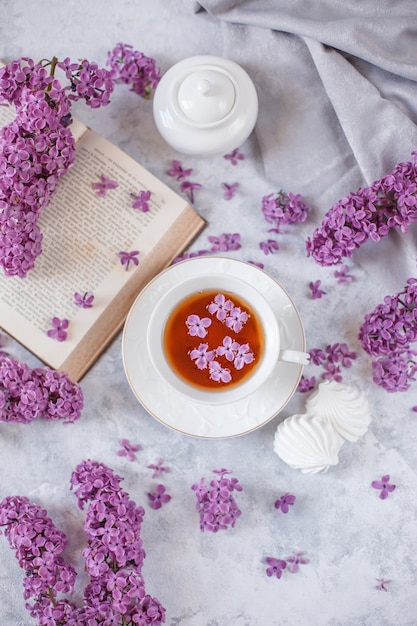 Una taza de té, merengue, ramas de lilas en flor y un libro viejo