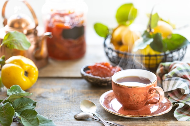 Taza de té con mermelada de membrillo casera en una vieja mesa de madera. Frutas frescas y hojas de membrillo