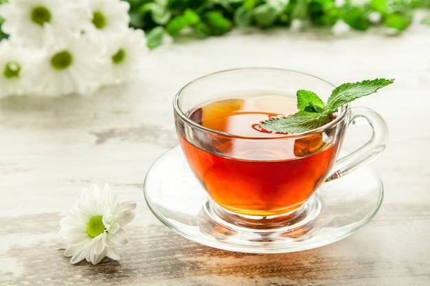 Taza de té en una mesa de madera con una flor y hojas de menta.