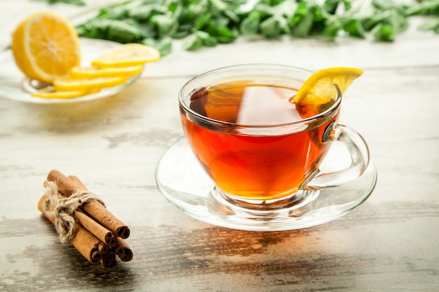 Taza de té en una mesa de madera con rodajas de limón y canela.