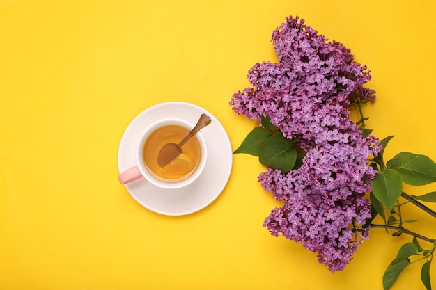 Taza de té negro aromático con limón y ramas de lilas florecientes sobre fondo amarillo Vista superior Lay Flat