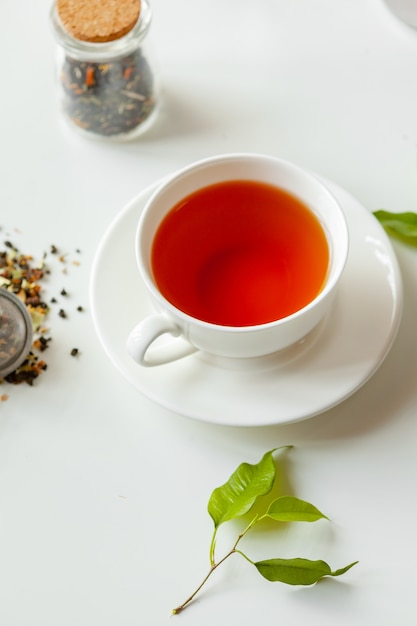 Taza de té negro caliente en la mesa blanca con tarro de té seco