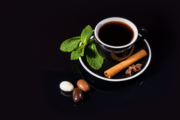 Taza de té negro con caramelo de chocolate y vainilla junto a aromas sobre fondo negro sólido