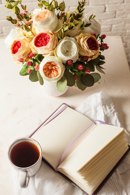 Una taza de té negro, cuaderno y hermosas flores sobre la mesa. Inspiración matutina para la planificación del día.