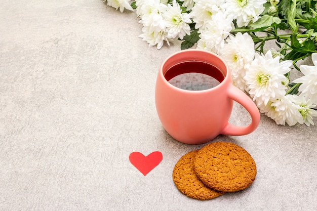 Taza de té negro, galletas de avena y ramo de crisantemos