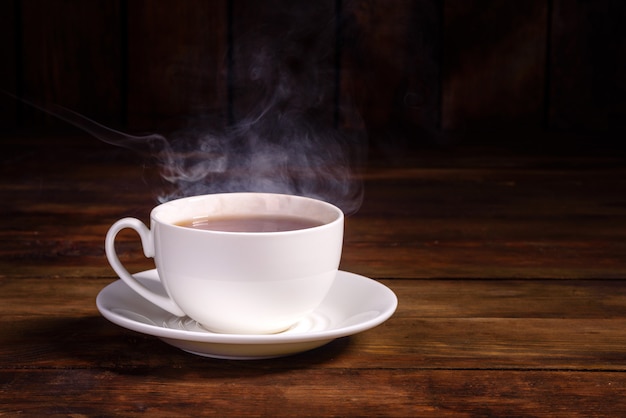 Una taza de té negro recién hecho, vapor que escapa, luz cálida y suave