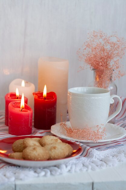 taza de té negro sobre un mantel a rayas, velas de cera, un jarrón de vidrio con hierbas decorativas