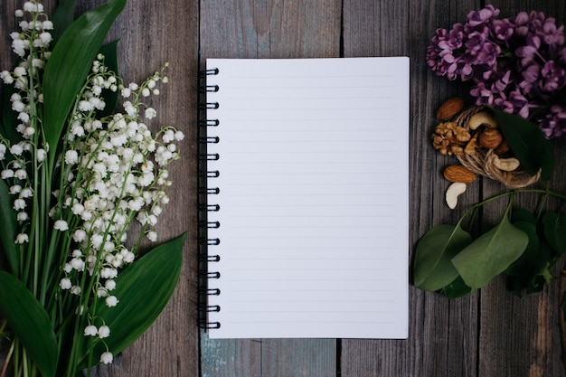 Una taza de té, nueces, lilas y un cuaderno sobre un fondo de madera