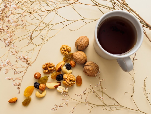 Taza de té, nueces y pasas junto a flores secas