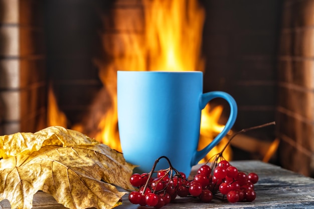 Taza de té o café y hojas de otoño antes de la acogedora chimenea en la casa de campo