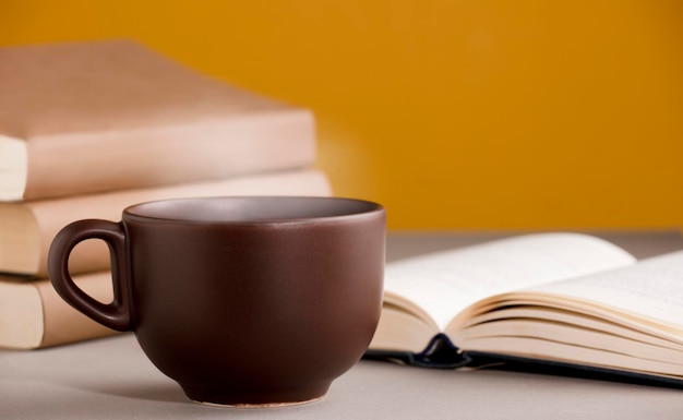 Taza de té o café marrón humeante caliente en el escritorio con libro abierto y fondo amarillo anaranjado