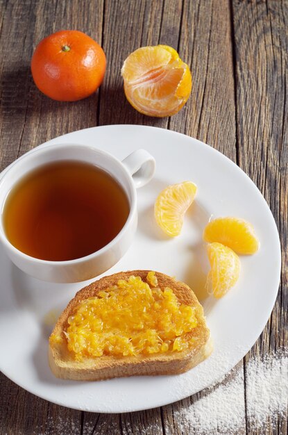 Taza de té y pan tostado con mermelada de mandarina en plato sobre mesa de madera rústica, vista de ángulo alto