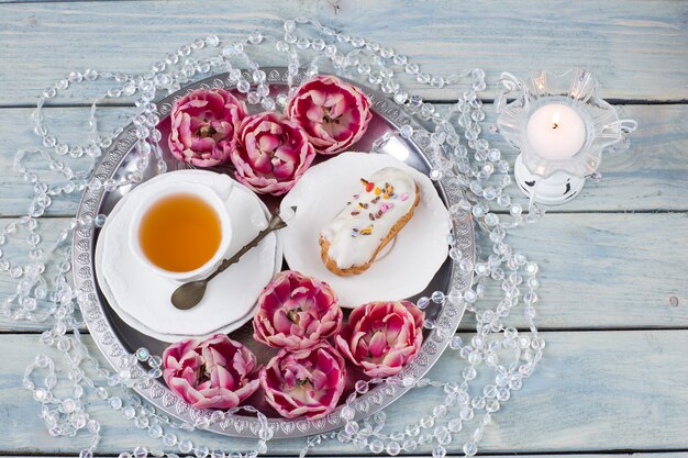 Taza de té, pastel, cuentas, un candelabro con una vela y siete capullos de tulipán