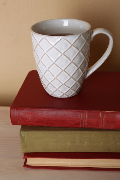 Taza de té con una pila de libros sobre una mesa de madera sobre fondo de pared claro