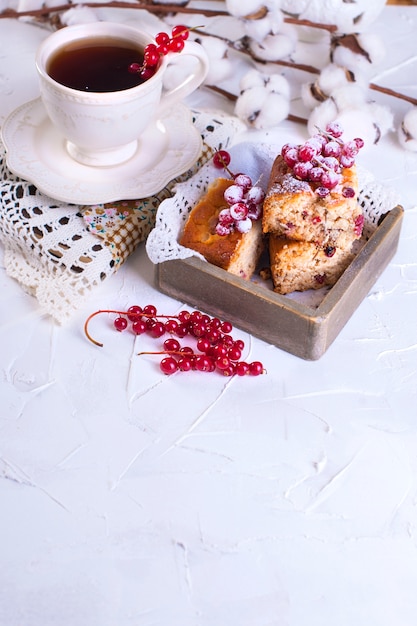 taza de té y platillo, cupcake con grosella roja sobre tabla de madera y fondo blanco, flores de algodón