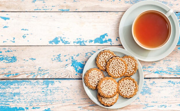 Taza de té y platillo con galletas en la mesa. Cima. vista.