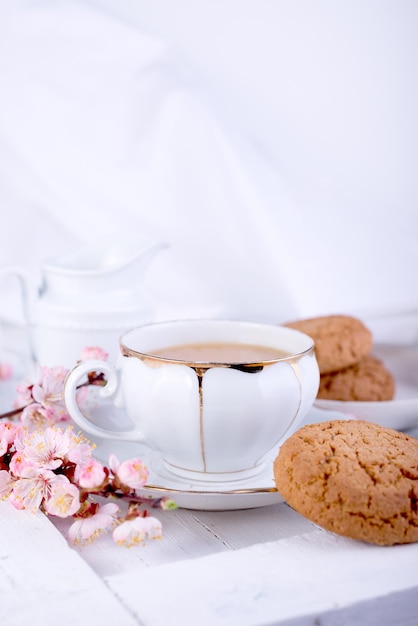 Taza de té de porcelana blanca jarra de leche y galletas de avena recién horneadas Desayuno inglés bodegón con bebida y golosinas y mantel