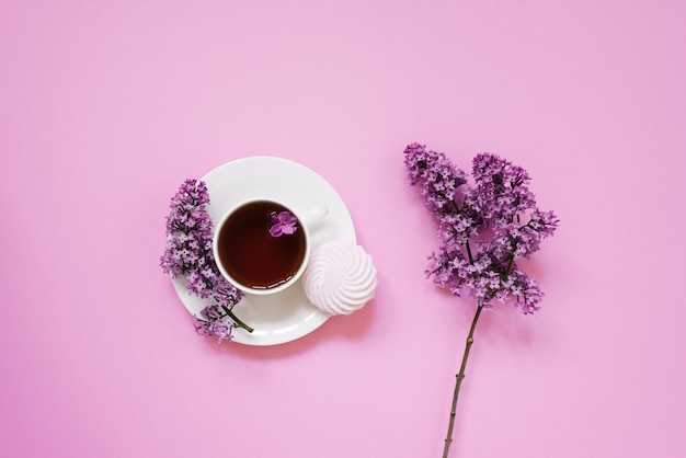 Taza de té con postre de malvavisco y flores lilas sobre un fondo rosa