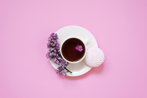 Taza de té con postre de malvavisco y flores lilas sobre un fondo rosa