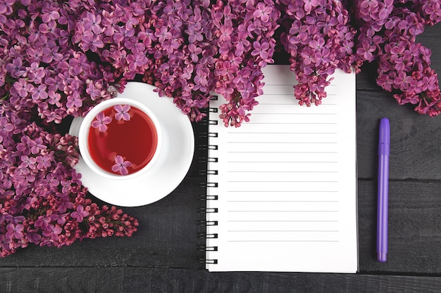 Taza de té y ramas de flores de primavera ramo lila floreciente en mesa negro. Cuaderno diario de mujer.