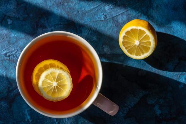 Una taza con té y rodajas de limón flotando sobre un fondo azul.