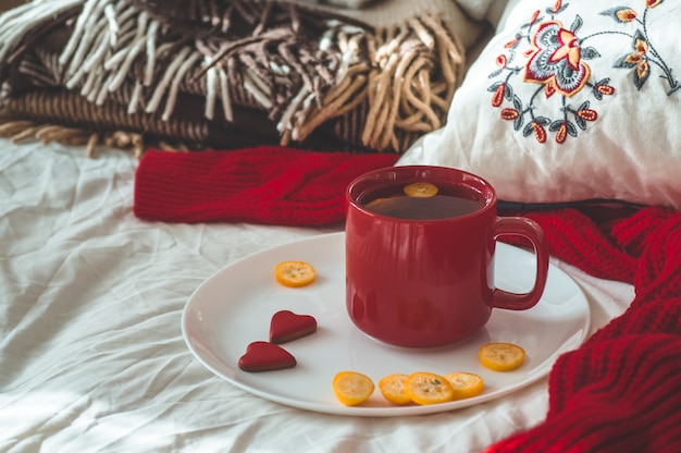 Taza de té rojo con kumquat y galletas de dos corazones sobre una cama blanca