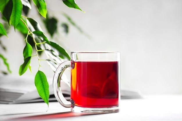 Una taza con té rojo sobre un fondo gris claro, junto a un libro