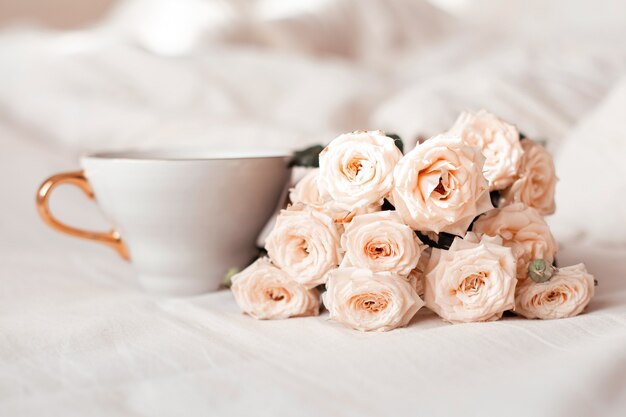 Taza de té y rosas blancas en el fondo de la cama