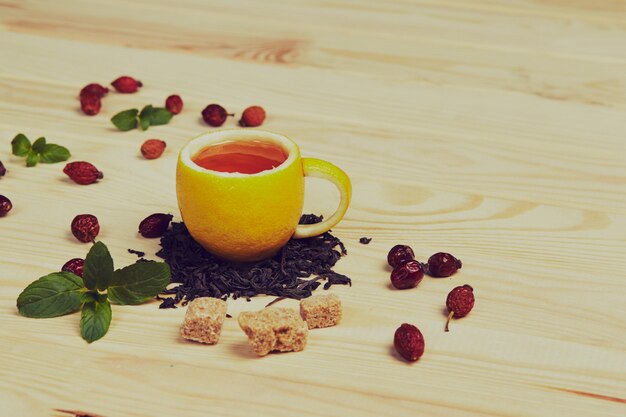 Taza de té con rosas de cadera, en mesa de madera. Una taza hecha de limón real