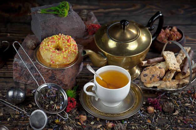 Una taza de té se sienta en una mesa con una tetera y otros alimentos.