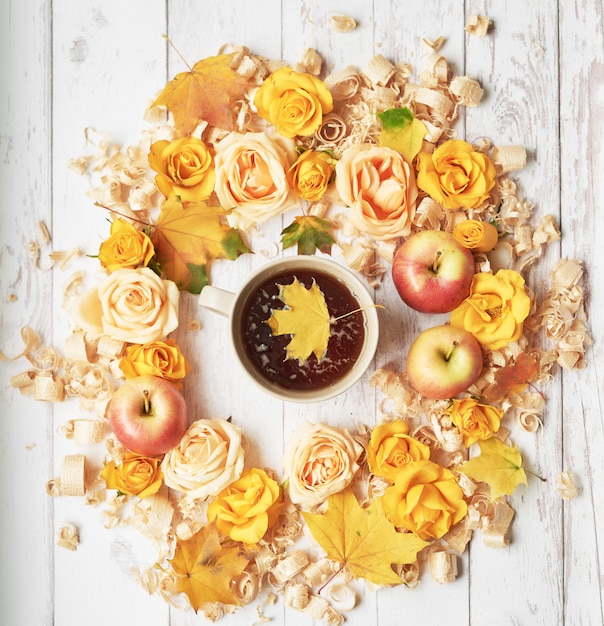 Taza con té sobre un fondo de otoño con manzanas, hojas y flores.