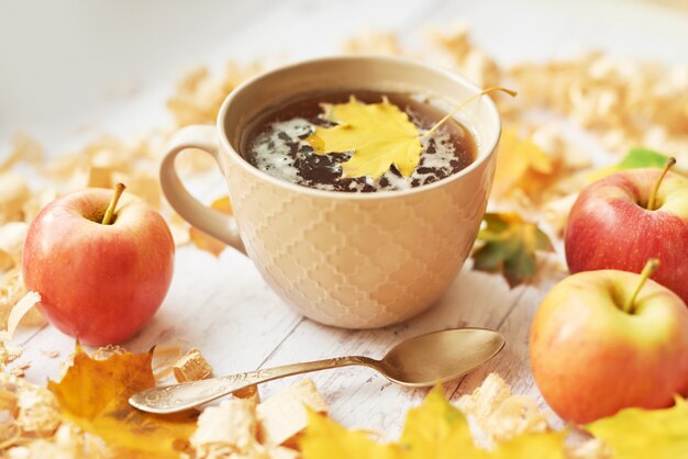 Taza con té sobre un fondo de otoño con manzanas, hojas y flores.